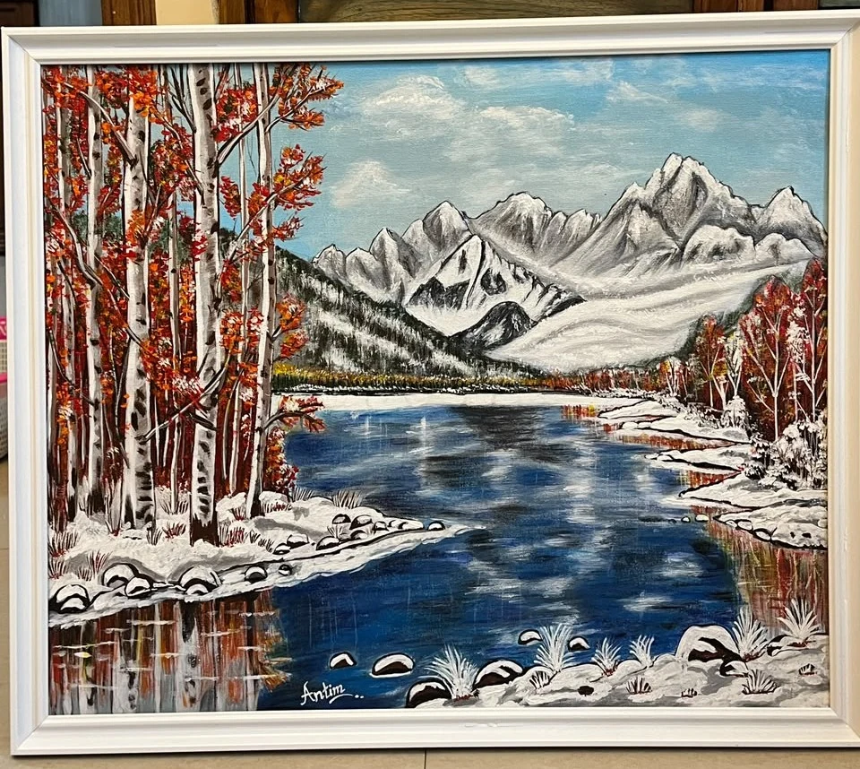 Snow-covered mountains and birch trees with red leaves beside a reflective blue lake, in a white frame.